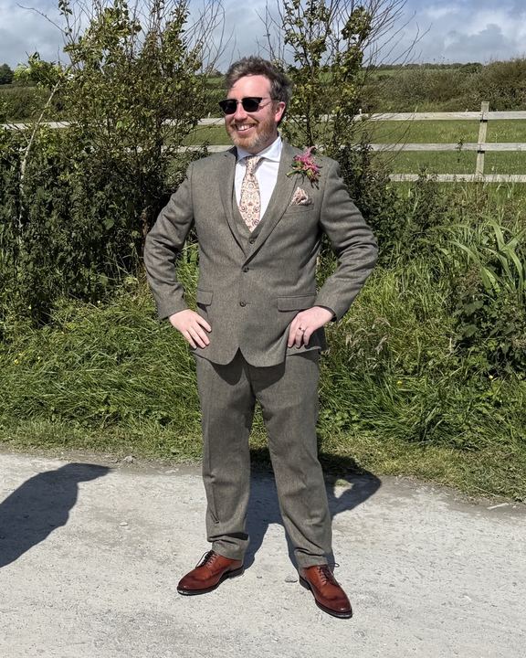 Ryan in a tweed three-piece suit, hands on hips, on a country lane